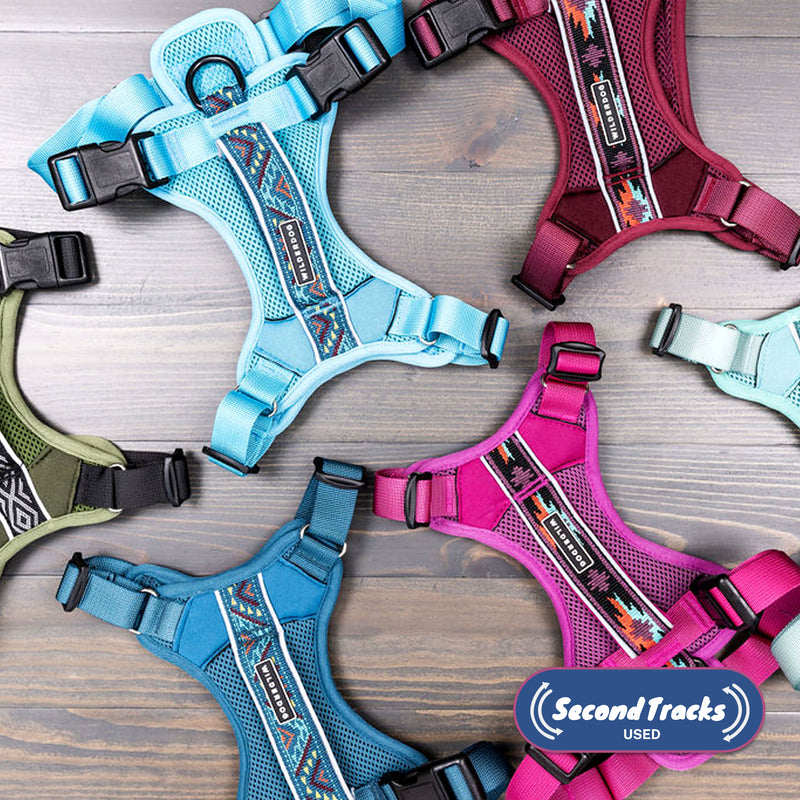 (Used) Harnesses in blue, teal, pink, burgundy, and green with patterned straps are displayed in a circle on wood. The "Second Track" logo appears in the lower right corner.